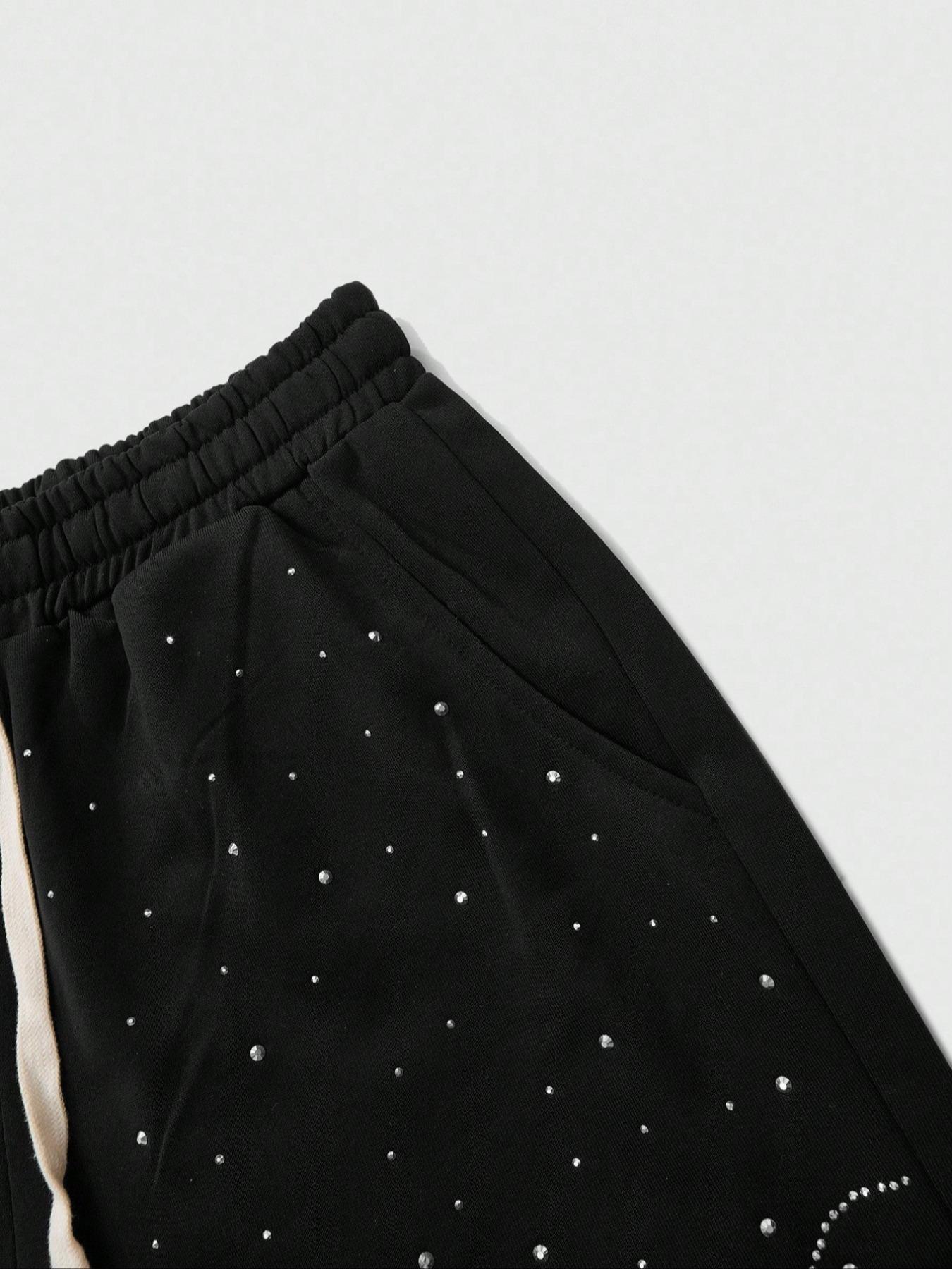 This men's two-piece set features a gothic streetwear design, including a long-sleeved T-shirt with a shimmering flame print and black flared trousers adorned with rhinestones and lettering.