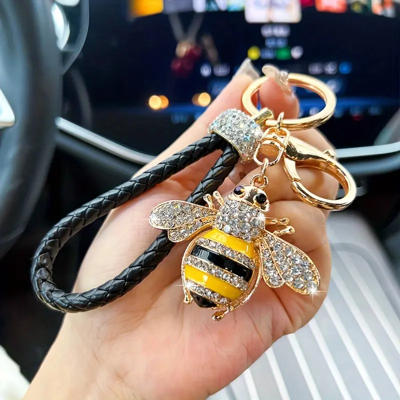 A Stylish Bee Keychain Adorned with Sparkling Diamond Accents - Featuring a Black And Golden Woven Cord, Made of Brass, It Makes a Perfect Little Gift Suitable for Decorating Bags Or Cars, a Delightful Bee-Themed Present