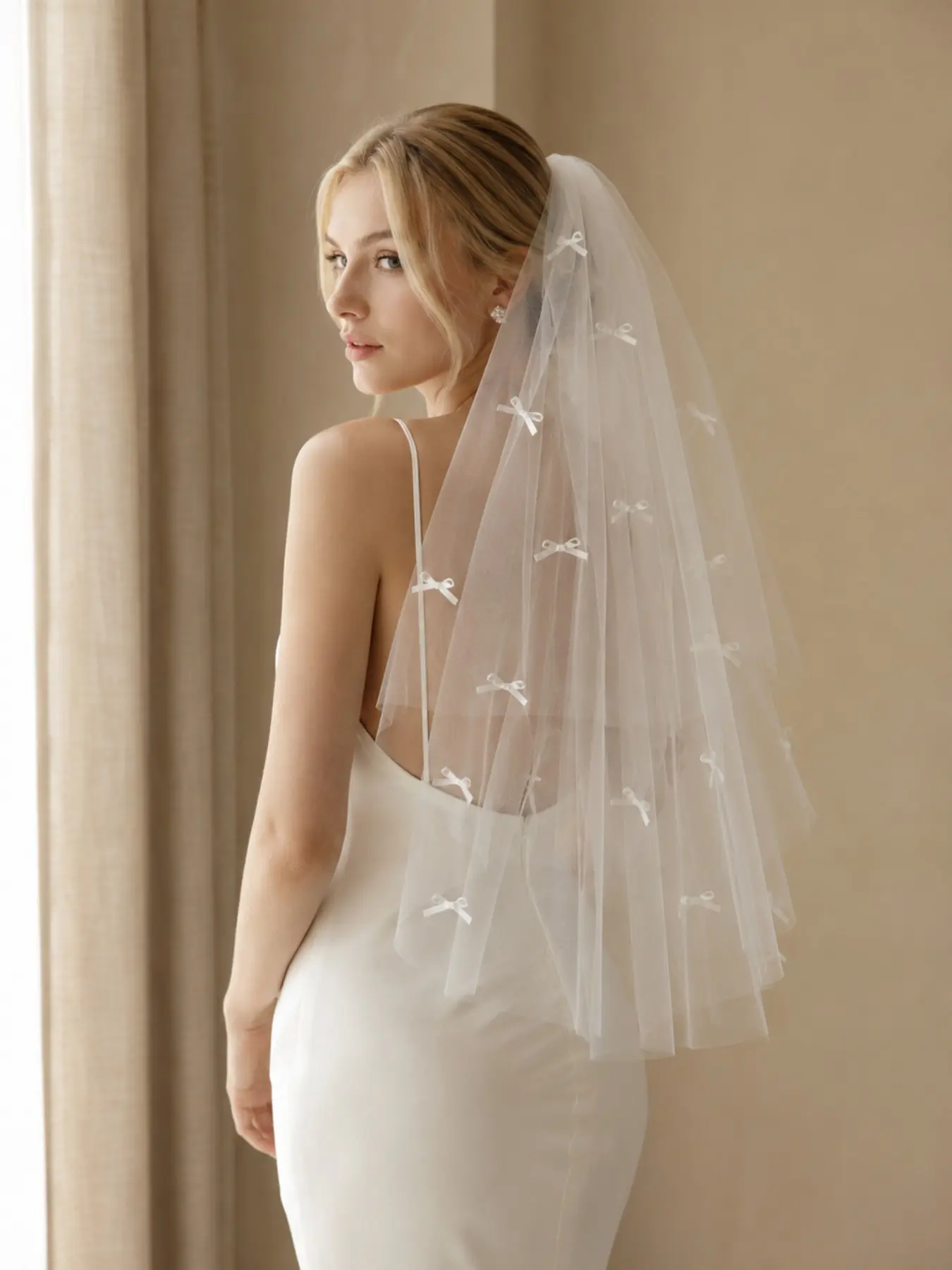 A dreamy, 85cm, double-layered, handmade Korean-style bridal veil featuring scattered, hand-stitched ribbon bows; this light and airy tulle veil is the perfect accessory for engagement and outdoor wedding photos.