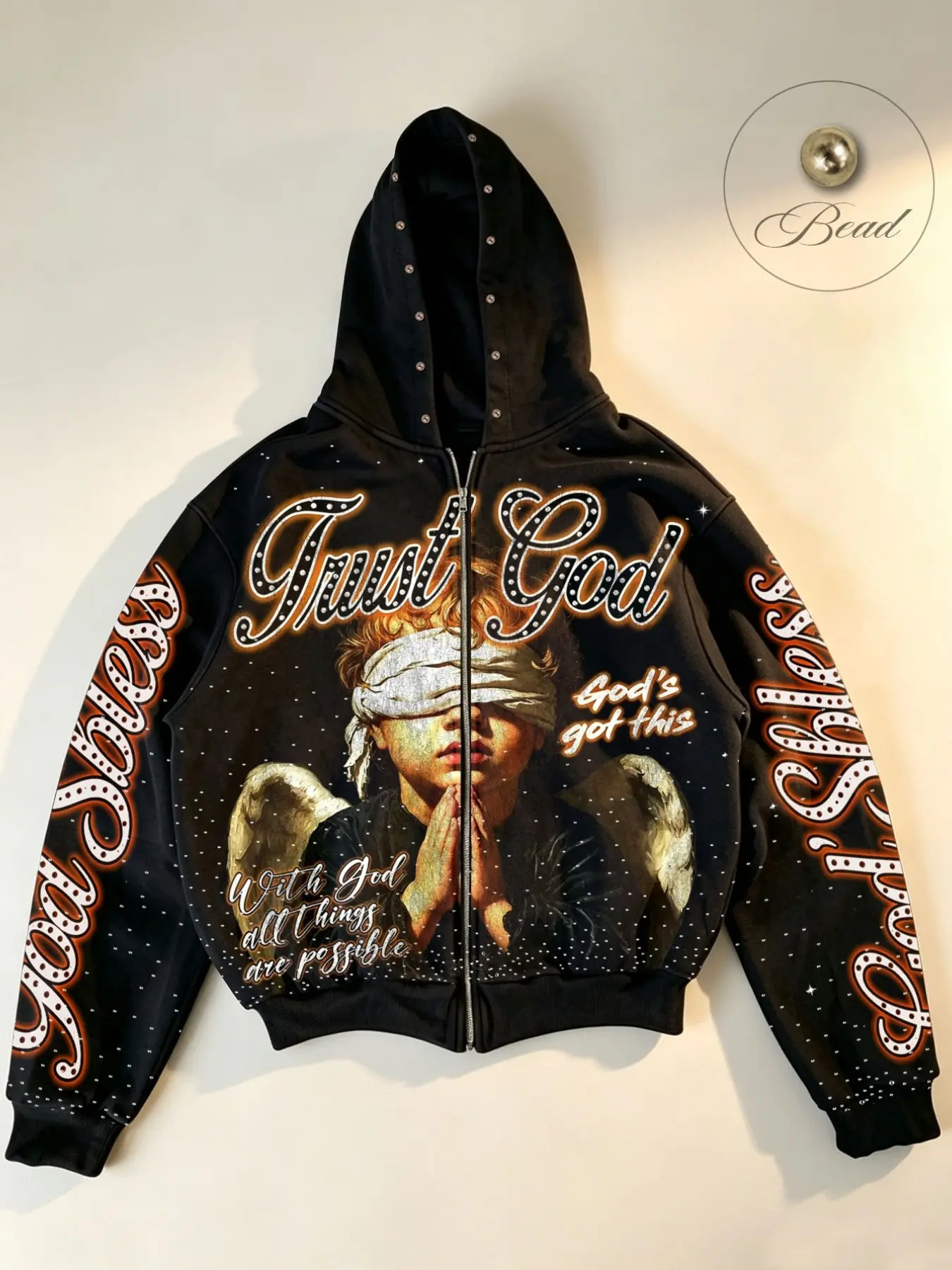 Unisex vintage-style zip-up hooded sweatshirt featuring a "Trust God" graphic print and "God's Bless" lettering on the sleeve. The design includes an all-over speckled pattern and bead embellishments on the hood brim. Loose