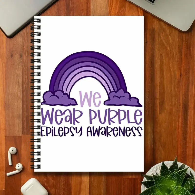 A purple spiral notebook with an epilepsy awareness theme, featuring a purple rainbow and clouds on the cover, along with the text "we wear purple epilepsy awareness." Suitable for work and study records, daily planning, and also great for use as a diary