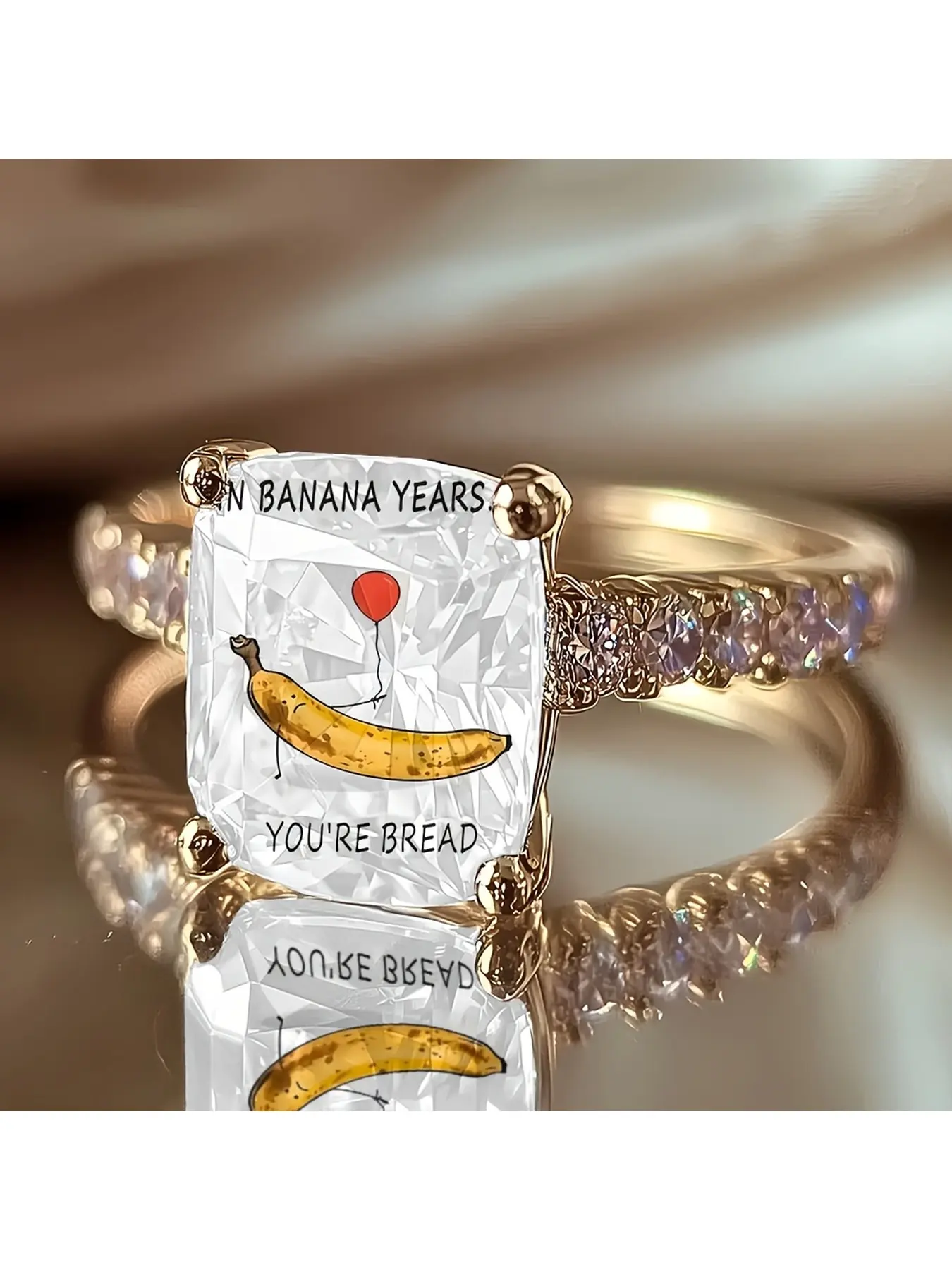Cartoon banana fun slogan printed ring, with a transparent rectangular cut surface, featuring an illustrated cartoon banana figure holding a red balloon, accompanied by an English fun slogan text.