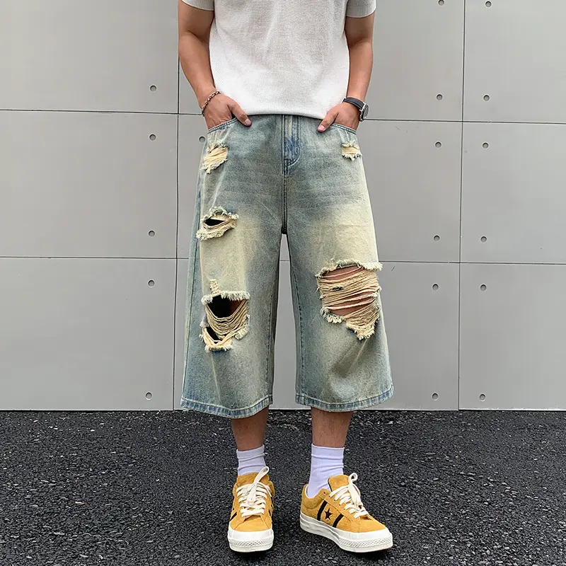 Vintage washed ripped denim jorts, multi frayed hole distressed detailing, classic button waist closure, loose wide knee-length silhouette, thick washed denim fabric, retro streetwear casual denim shorts for summer daily layered outfits