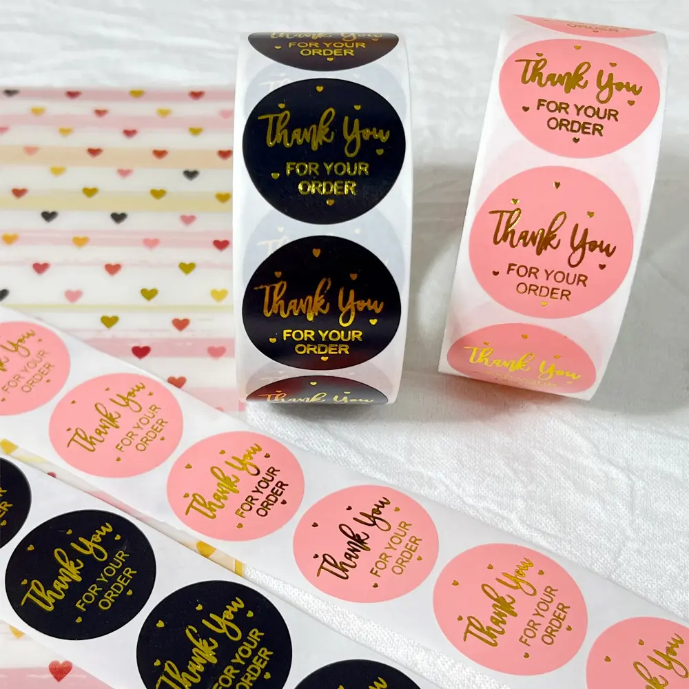 2 rolls of gold-stamped pink and black thank-you stickers in round roll form, for decorating the seals of wedding and festival envelopes. 500 pieces per roll.