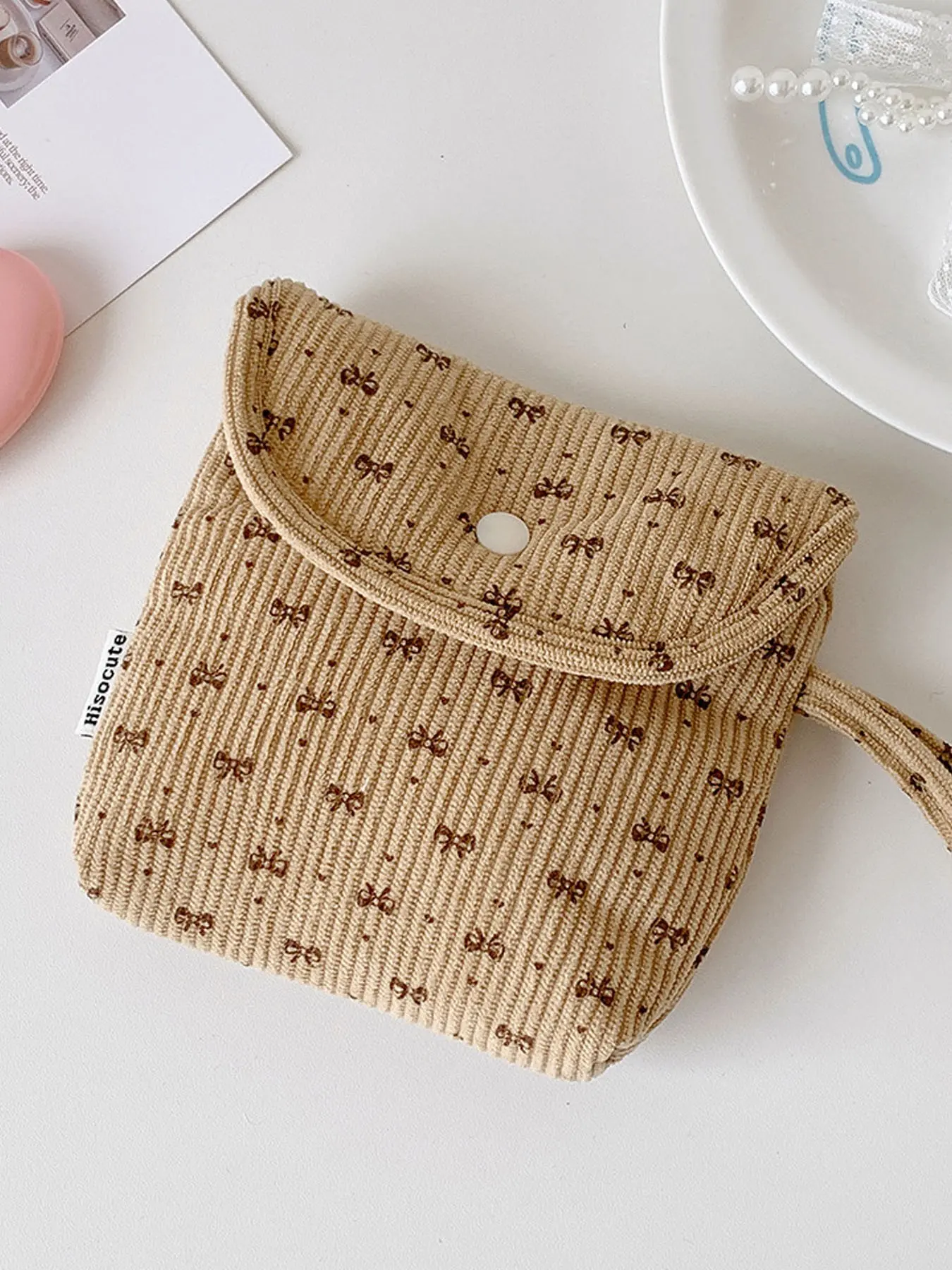 Beige bow print corduroy mini pouch with snap closure and wrist strap, soft textured fabric. Compact size holds sanitary napkins, lipsticks and earbuds. Cute pattern design, lightweight and portable for daily use, travel or school. Wristlet Pouch