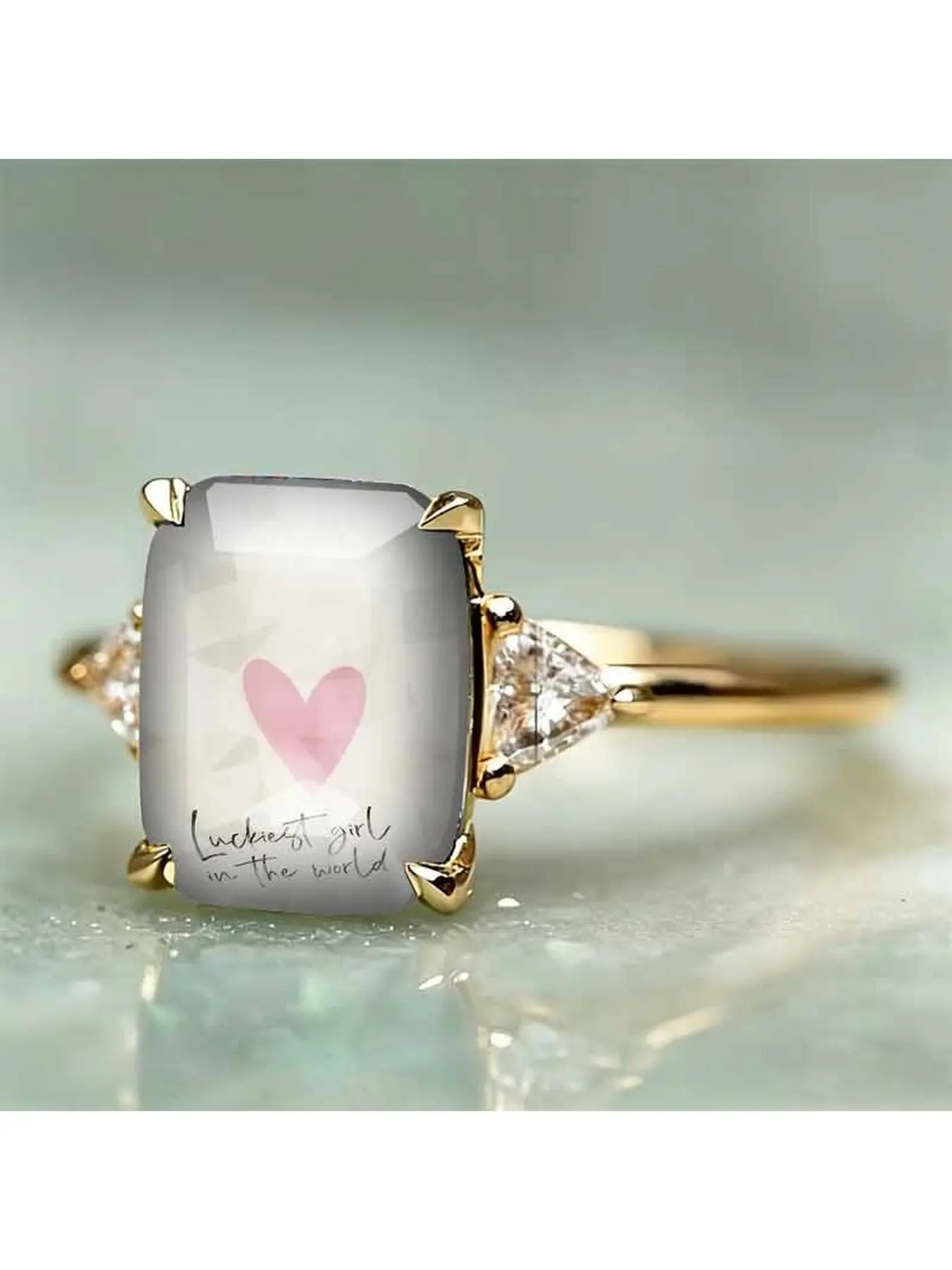 Soft pink heart-shaped hand-painted English print square ring. The inscription reads "The luckiest girl in the world". It features a simple, gentle, light color scheme, with a romantic and soothing meaning. It is suitable as a gift for couples and is a re