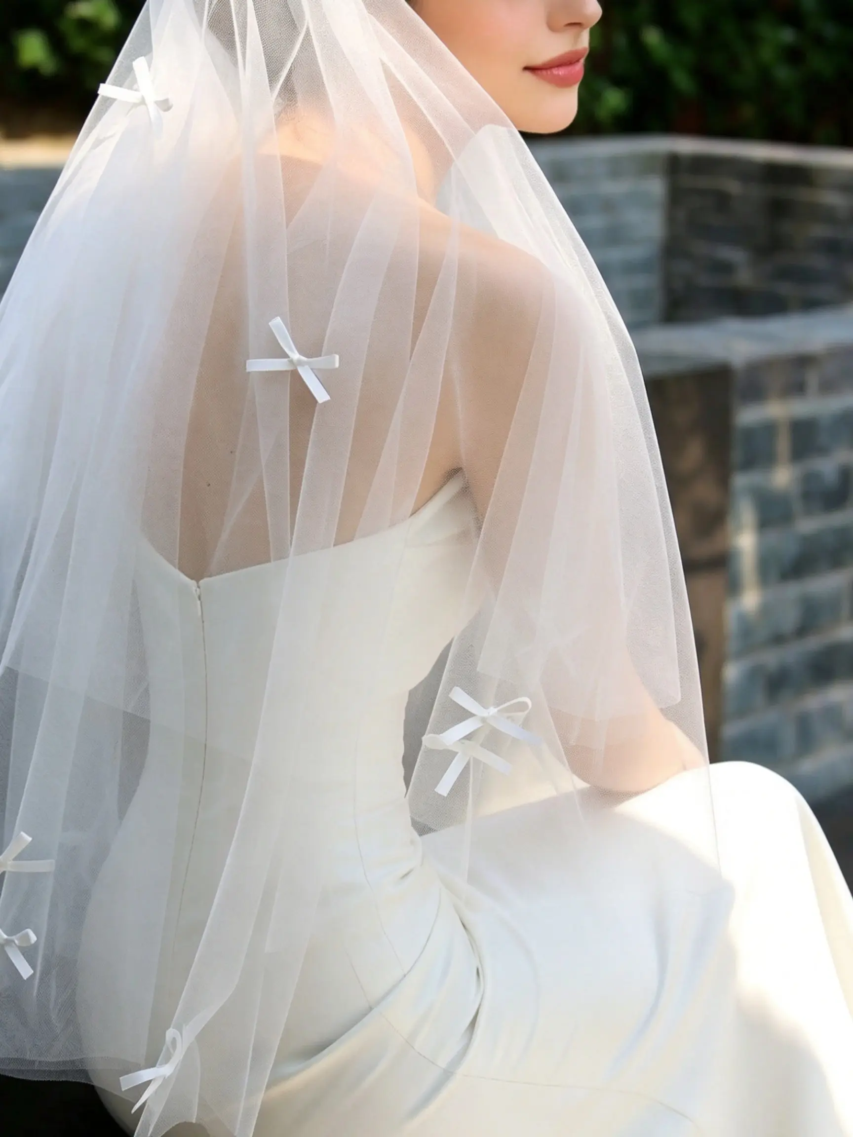 A dreamy, 85cm, double-layered, handmade Korean-style bridal veil featuring scattered, hand-stitched ribbon bows; this light and airy tulle veil is the perfect accessory for engagement and outdoor wedding photos.
