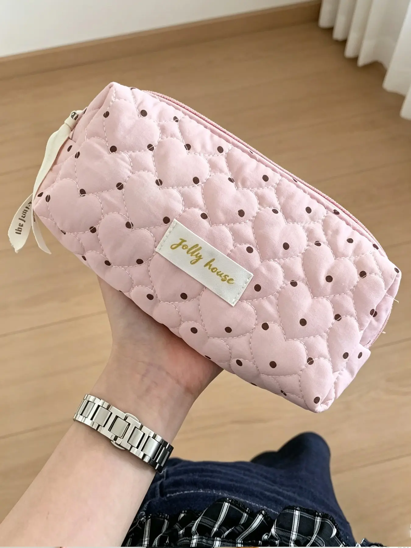 Quilted cosmetic bag with pink polka dot heart patterns, equipped with decorative webbing zipper pulls. This portable travel makeup storage pouch can hold skin care products and makeup tools, with multiple sizes available.