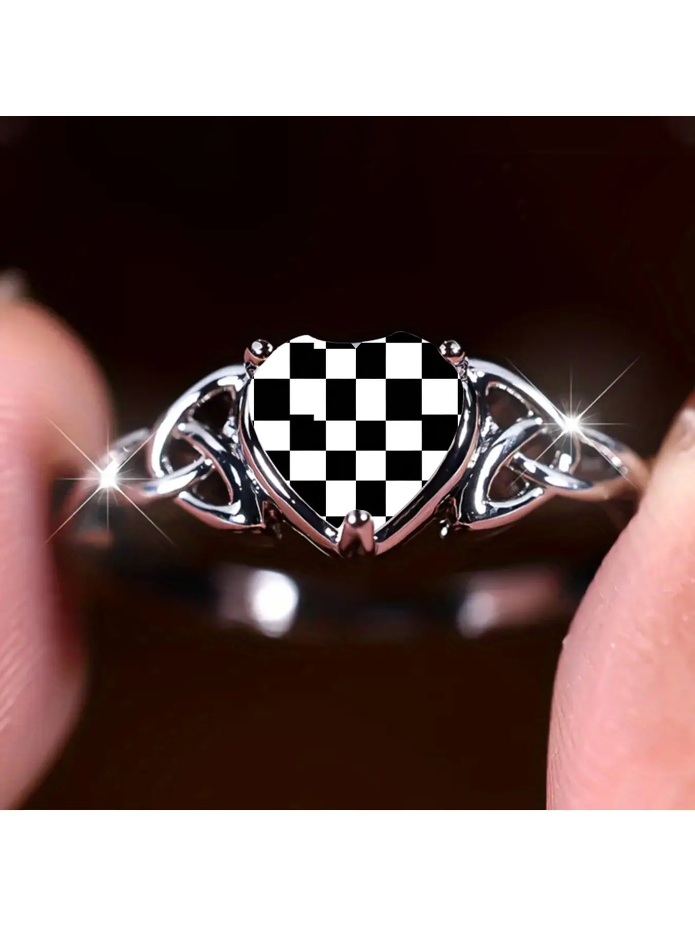 A black and white checkered heart-shaped ring with symmetrical Celtic knot hollow designs on both sides of the ring body. The main heart-shaped stone is covered with classic black and white square patterns. It has a simple, cool and retro style, suitable